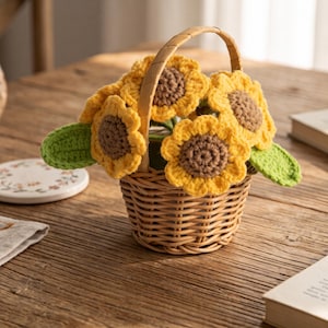 Op de afbeelding: Een kleine, ronde, lichtbruine gevlochten rieten mand met een enkel gebogen handvat, met daarin verschillende gehaakte zonnebloemen met felgele bloemblaadjes en donkerbruine harten, geaccentueerd door twee felgroene gehaakte bladeren aan de zijkanten.