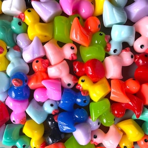 May include: A collection of colorful, miniature duck figurines in various shades of pink, yellow, blue, green, orange, and red. Each duck has a small, round black eye and a red beak. The ducks are arranged closely together, creating a vibrant and playful display.