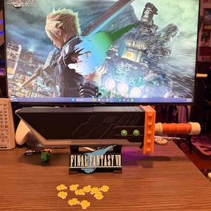 Könnte beinhalten: Eine schwarze und orangefarbene Buster Sword-Replik aus Final Fantasy VII, mit einem Ständer mit der Aufschrift "Final Fantasy VII". Das Schwert liegt auf einer Holzoberfläche, mit gelben blütenförmigen Dekorationen.