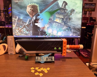 May include: A black and orange Buster Sword replica from Final Fantasy VII, with a stand that reads "Final Fantasy VII". The sword is on a wooden surface, with yellow flower-shaped decorations.