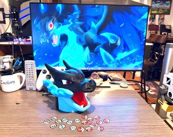 May include: A black, red, and light blue Charizard-themed figurine with a wide open mouth, and a set of small, round, colorful game tokens. A computer monitor displays a blue dragon graphic.