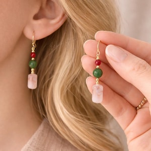 Op de afbeelding: Gouden oorhangers met rode, groene en roze edelstenen. De oorbellen hebben een gouden haak en kleine gouden kralen tussen de edelstenen. De edelstenen hebben ronde en rechthoekige vormen.