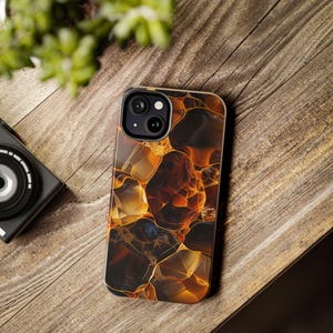Op de afbeelding: Een smartphonehoesje met een abstract ontwerp. Het hoesje heeft een patroon van amberkleurige, bruine en gouden vormen, waardoor het op een edelsteen lijkt. De hoes is ontworpen voor een smartphone en heeft uitsparingen voor de camera en andere functies.
