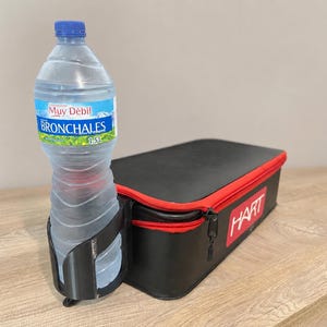 May include: A black rectangular storage case with a red zipper and the white text HART printed on the side. A black plastic cup holder is attached to the side, holding a clear 1.5-liter plastic water bottle with a blue cap and label.