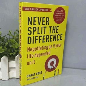Könnte beinhalten: Ein gelbes Buch mit dem Titel "Never Split the Difference" von Chris Voss. Das Buchcover zeigt einen großen schwarzen Text und den Untertitel "Verhandeln, als ob Ihr Leben davon abhängt". Ein roter Kreis mit einer Zielscheibengrafik ist ebenfalls sichtbar.