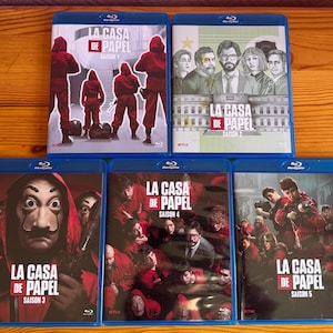 Peut inclure: Cinq boîtiers de disques Blu-ray pour la série télévisée "La Casa de Papel" (Money Heist). Les boîtiers bleus affichent le titre de la série et les numéros de saison en blanc et rouge. Les couvertures présentent des images des personnages en combinaisons rouges et masques.