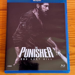 Peut inclure: Boîtier Blu-ray bleu avec le film "The Punisher: One Last Kill". La couverture montre un homme en sweat à capuche noir tenant une batte de baseball. Le logo Blu-ray est en haut.