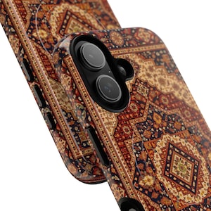 May include: Close-up of a phone case with a detailed, ornate pattern reminiscent of a Persian rug. The case features a rich color palette of red, navy, beige, and gold, with intricate floral and geometric designs. The phone's camera lenses are visible.