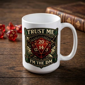 Puede incluir: Una taza de cerámica blanca con un gráfico de un dado rojo de veinte caras centrado en un diseño de estandarte verde oscuro y dorado. El texto "TRUST ME" aparece en la parte superior y "I'M THE DM" en la parte inferior en negrita.