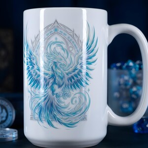 Peut inclure: Un mug en céramique blanche orné d'une illustration détaillée d'un phénix aux ailes déployées dans des tons bleu et argent. L'oiseau est centré dans un cadre arqué décoratif, avec des détails de plumes complexes et des plumes de queue fluides.