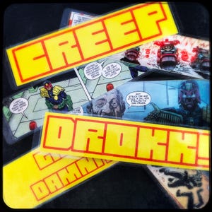 Może przedstawiać: Kolekcja żółtych i czerwonych naklejek z panelami komiksowymi i tekstem. Naklejki zawierają słowa "GREEP" i "DROKK!" dużymi, pogrubionymi literami. Panele komiksowe przedstawiają postać w hełmie i inne postacie.