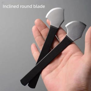 May include: Two inclined round blade tools with black handles and silver blades are held in a hand. The text "Inclined round blade" is in the upper left corner. The blades have a curved shape.