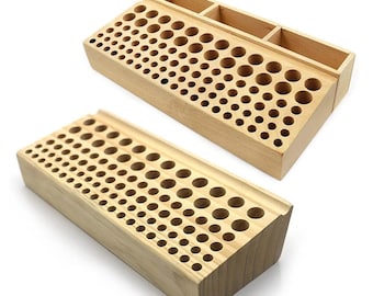 Puede incluir: Dos organizadores rectangulares de madera clara con múltiples orificios circulares de diámetros variables dispuestos en filas. Uno de los organizadores cuenta con una sección superior adicional con tres compartimentos rectangulares abiertos.