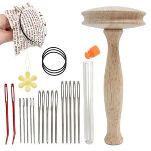 May include: A wooden darning mushroom tool, a clear plastic needle case with an orange cap, three black elastic bands, a yellow flower-shaped needle threader, and a collection of metal sewing needles including two curved red needles.