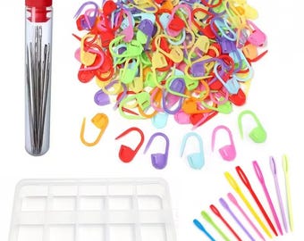 Puede incluir: Una colección de marcadores de puntos de plástico multicolor, un tubo cilíndrico transparente con agujas de coser de metal plateado y tapa roja, una caja de almacenamiento de plástico transparente con compartimentos y agujas de plástico largas.
