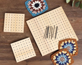 Puede incluir: Un conjunto de tres tablas de bloqueo cuadradas de madera con orificios, acompañadas de varios pasadores metálicos. Tres cuadrados de ganchillo en tonos azul, marrón, crema y amarillo se sitúan cerca de las tablas sobre madera oscura.