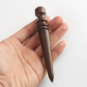 May include: A dark brown wooden leather burnisher tool featuring a rounded top, a series of three distinct horizontal grooves along the upper section, and a tapered, pointed end designed for smoothing and finishing leather edges.
