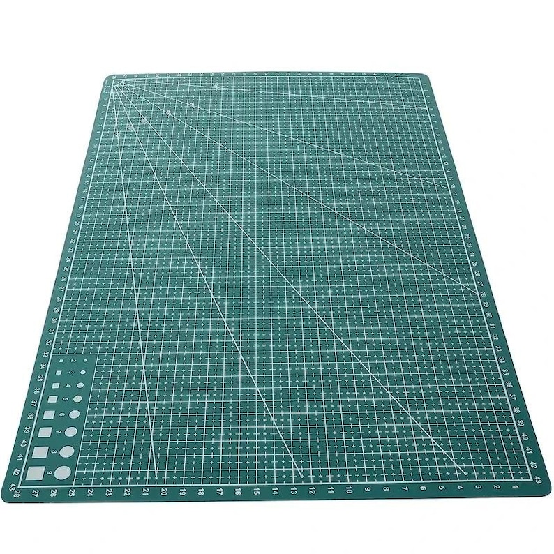 K&ouml;nnte beinhalten: Eine gr&uuml;ne Schneidematte mit wei&szlig;en Gitterlinien und Ma&szlig;angaben. Die Matte hat diagonale Linien und Zahlen entlang der Kanten, mit Messungen bis zu 109 cm. Ideal f&uuml;r Bastel- und N&auml;hprojekte.