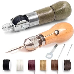 Könnte beinhalten: Zwei Leder-Nähahlen mit Holzgriffen, einer mit dunkelgrünem Finish und einer mit naturfarbenem hellem Holz. Das Set enthält einen kleinen Metallschlüssel, zwei Ersatznadeln und sechs Garnrollen in Schwarz, Weiß, Burgunderrot, Beige, Braun und Dunkelbraun.