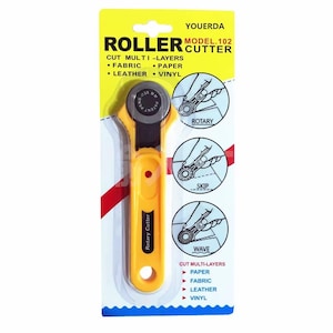 May include: Yellow and black rotary cutter for fabric, paper, leather, and vinyl. The package includes the text "ROLLER CUTTER" and "CUT MULTI-LAYERS". The cutter has a yellow handle and a silver blade. The package also shows different cutting styles.
