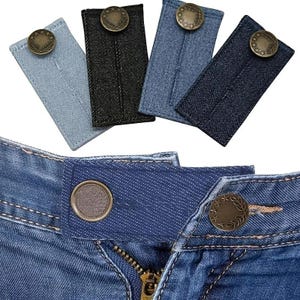 May include: A close-up of denim jean extenders in various shades of blue and black. Each extender has a metal button with a decorative design. One extender is attached to a pair of blue jeans, showing the button and zipper.