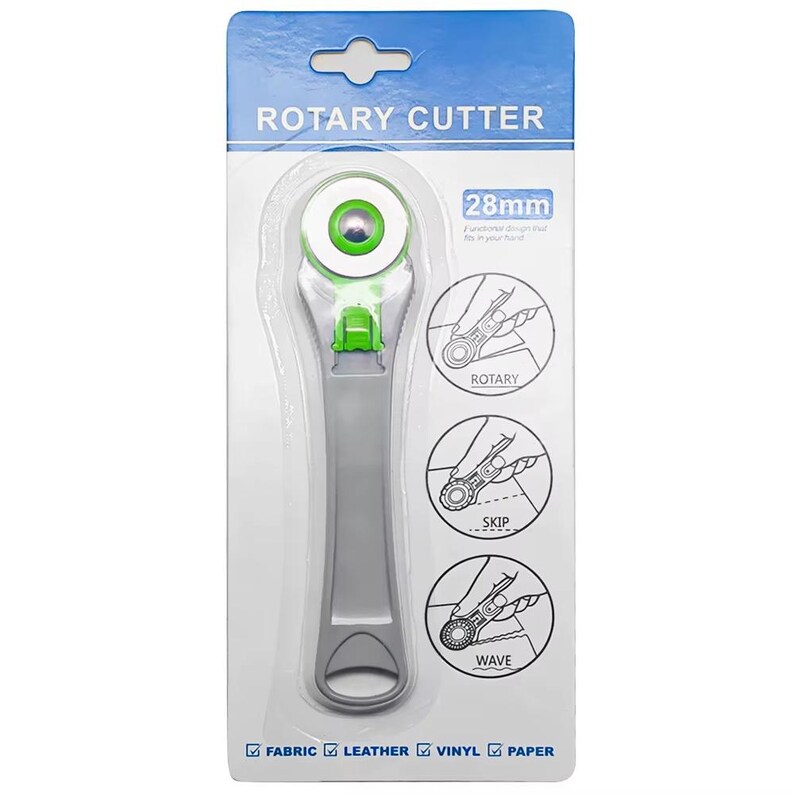 May include: A gray and green rotary cutter in a clear plastic package. The package has the words "ROTARY CUTTER" and "28mm" printed on it. The cutter is designed for fabric, leather, vinyl, and paper.