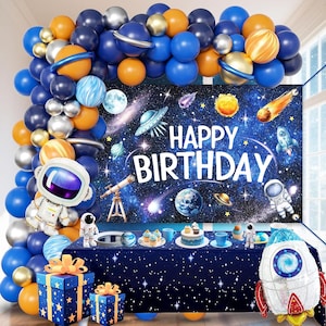 May include: A space-themed birthday party setup with a backdrop that reads "Happy Birthday." The scene includes blue, orange, and silver balloons, a table with space-themed decorations, gifts, and a rocket-shaped balloon.