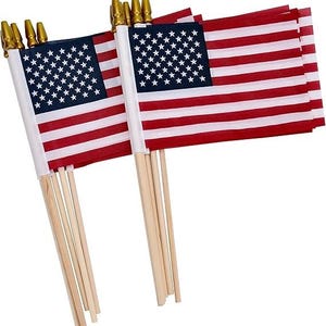 May include: Several miniature American flags. Each flag features a blue canton with white stars and red and white stripes. The flags are attached to wooden dowels with gold-colored tips. The flags are suitable for patriotic displays.