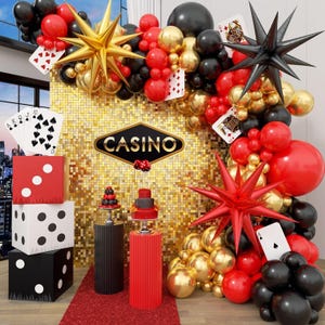 Puede incluir: Una decoración de fiesta con temática de casino que incluye un fondo de lentejuelas doradas con un letrero de Casino, un arco de globos en rojo, negro y dorado con globos de estrella, cajas de dados grandes, naipes y dos pedestales cilíndricos.
