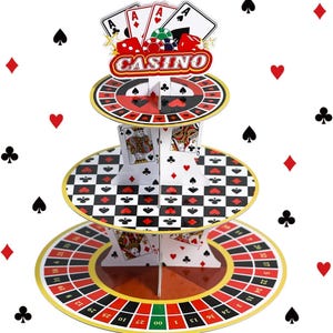 Puede incluir: Un soporte para cupcakes de tres niveles hecho de cartón con temática de casino. El nivel superior muestra cartas de juego y dados con la palabra CASINO. El nivel medio tiene un patrón de cuadros blanco y negro. La base es una ruleta.