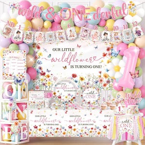 May include: A first birthday party decoration set featuring a wildflower theme with pastel balloons, a banner with photos from months 1 to 12, a large number one balloon, floral plates, a tablecloth, and white blocks spelling out the word ONE.