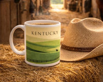 May include: A white ceramic mug with the word "Kentucky" and a landscape design, filled with coffee, sits on a bale of hay next to a straw cowboy hat. The background shows a barn with horses.