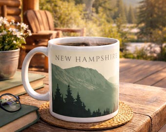 May include: A white ceramic mug filled with coffee, featuring a mountain and forest design with the text "NEW HAMPSHIRE". The mug sits on a wooden table with books and glasses, with a scenic outdoor background.