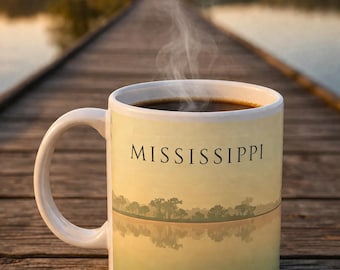 May include: White ceramic coffee mug filled with dark liquid, possibly coffee, with steam rising. The mug features the word "MISSISSIPPI" and a landscape scene of a lake and trees. The mug is on a wooden surface.
