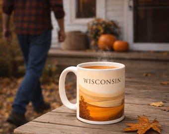 May include: A white ceramic mug with the word "WISCONSIN" printed on it, featuring a landscape design in shades of orange and brown. The mug sits on a wooden surface with a fallen leaf, with a person walking in the background.