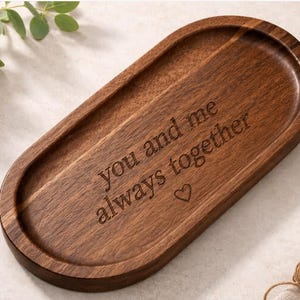 May include: A dark brown, oval wooden tray. The tray has the inscription "you and me always together" and a heart symbol carved into the wood. This decorative tray is a thoughtful gift.