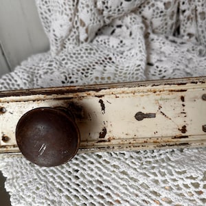 May include: An antique door knob and plate with a distressed, aged appearance. The knob is a dark brown, rounded shape, and the plate is rectangular with a keyhole and screw holes. The metal has a white finish with rust and wear.
