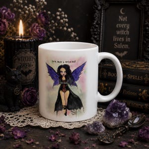 May include: A white ceramic mug featuring a printed illustration of a fairy with long black hair and purple wings. The fairy wears a black outfit and is positioned below the text "FAITH, TRUST & BITCH DUST" in a black, stylised font.
