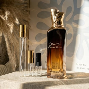 May include: A perfume bottle labeled "Vanilla Seduction" with a gold cap, alongside three smaller spray bottles. The perfume bottle has a gradient from dark brown to amber. The smaller bottles have gold or black caps.