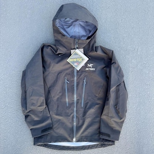 May include: A dark gray hooded jacket with a full-length zipper and multiple pockets. The jacket features the "GORE-TEX" and "Arc'teryx" logos. The jacket is designed for outdoor activities and protection from the elements.