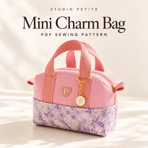 May include: A pink mini charm bag with a floral print base, featuring a gold zipper, two woven handles, and a heart-shaped patch with the letter P. A circular charm with the letter P hangs from the handle. Text reads STUDIO PETITE Mini Charm Bag PDF SEWING PATTERN.