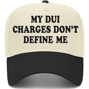 May include: A baseball cap with a cream-colored crown and a black brim. The cap features the text "MY DUI CHARGES DON'T DEFINE ME" in bold, black letters across the front.