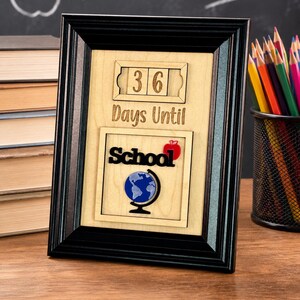 May include: A black framed wooden countdown sign featuring the text 36 Days Until School with a red apple icon and a blue globe graphic. The sign is designed with a light wood background and a mechanical number display for tracking days.