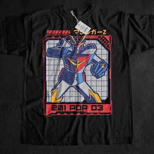 Pode incluir: Camiseta preta com um gráfico colorido de um robô em vermelho, branco, azul e amarelo. O design é emoldurado com linhas vermelhas e inclui texto japonês e o texto "201 POP 03". Uma etiqueta branca está anexada.