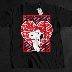 Puede incluir: Camiseta negra con un diseño de dibujos animados de Snoopy. Snoopy está dentro de un corazón lleno de corazones rojos, con un fondo cuadrado rojo que repite la palabra "LOVE". Una etiqueta dice "LARGE".