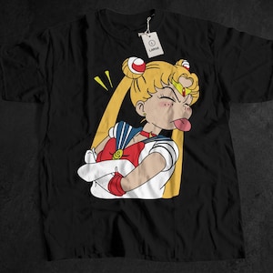 May include: Black t-shirt featuring a cartoon illustration of a character with blonde hair, red and white outfit, and a defiant expression. The character is sticking out their tongue. A white tag with the size "L" is attached.