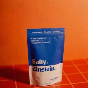 Könnte beinhalten: Ein blau-weißer Beutel mit "Salty Einstein" Blaubeer-Limonaden-Elektrolytpulver. Der Beutel enthält den Text "Lions Mane, Creatine, Minerals" und "Canadian Sea Salt". Der Hintergrund ist orange.