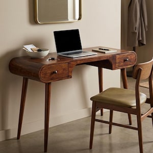 May include: A dark wood writing desk with rounded edges, two drawers with small knobs, and four tapered legs. A matching wooden chair with a light olive green upholstered seat is positioned in front of the desk. A laptop sits on the desk surface.