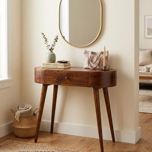 May include: A mid-century modern style console table with a dark wood finish, featuring a single drawer and tapered legs. Dimensions: W 31.5 inches, H 30.7 inches, D 15.7 inches. The table is accessorized with a mirror, vase, books, and a tote bag.