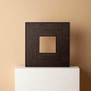 May include: A square, dark brown wooden picture frame with a lighter brown square center. The frame has a textured, wood-grain appearance and is displayed on a white surface against a neutral background.